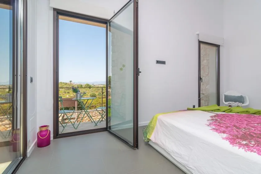 A bedroom opens onto a balcony with outdoor seating and a view of the landscape.