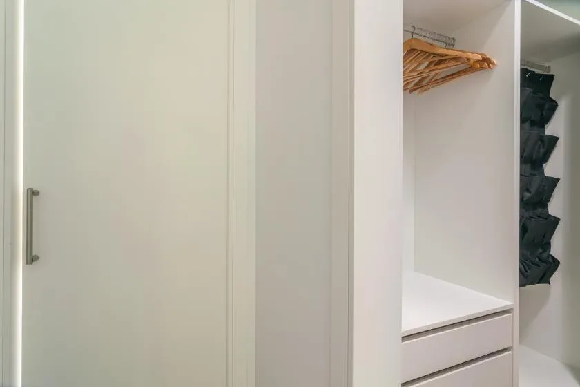 An open wardrobe with hanging clothes and shelves beside a closed door.