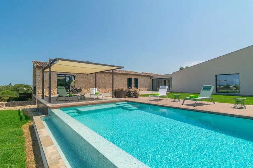 Outdoor swimming pool beside a brick building, with patio seating under a shaded canopy.