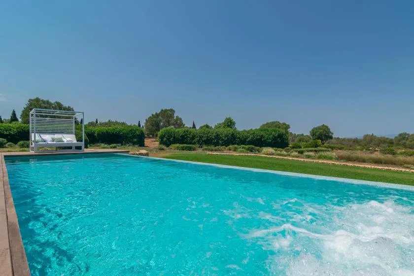 An outdoor swimming pool with clear blue water and greenery beyond.