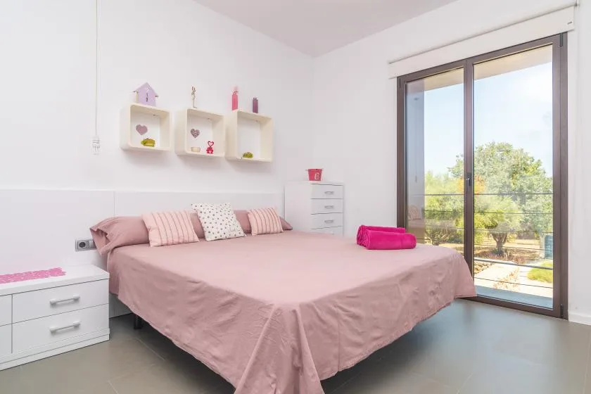 A pink bedroom with a neatly made bed and sliding glass doors opening to a balcony.