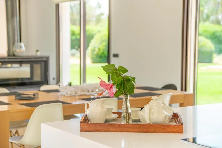 A bright dining area with a wooden table and a vase of greenery.