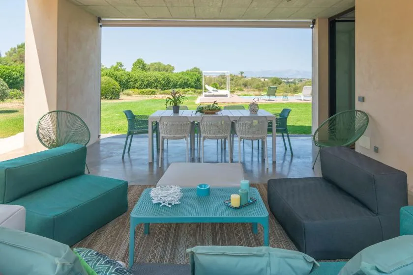 An open lounge and dining area faces a green lawn through a wide glass opening.