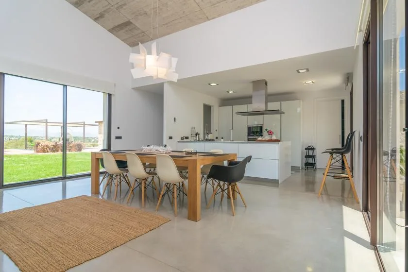 An open-plan dining area and kitchen with a long wooden table and large windows.