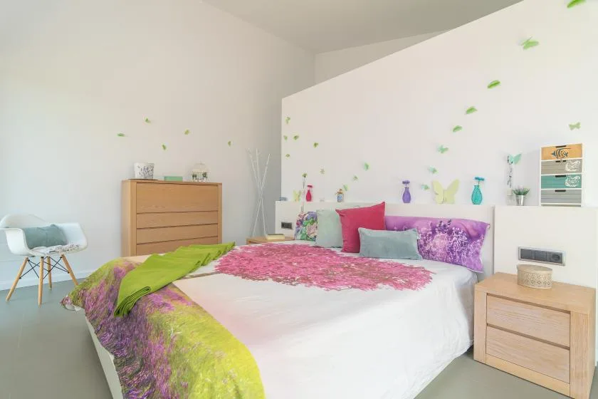 A bright bedroom with colorful bedding and light wood furniture.