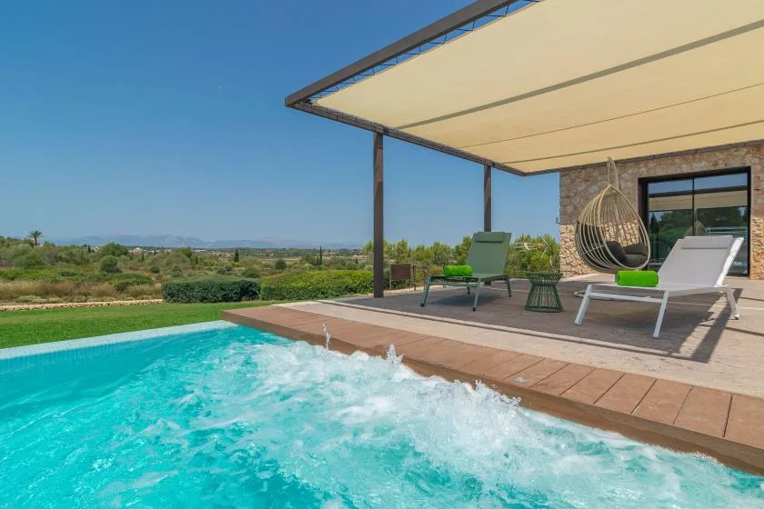 An outdoor pool beside a shaded patio with seating and a hanging chair.