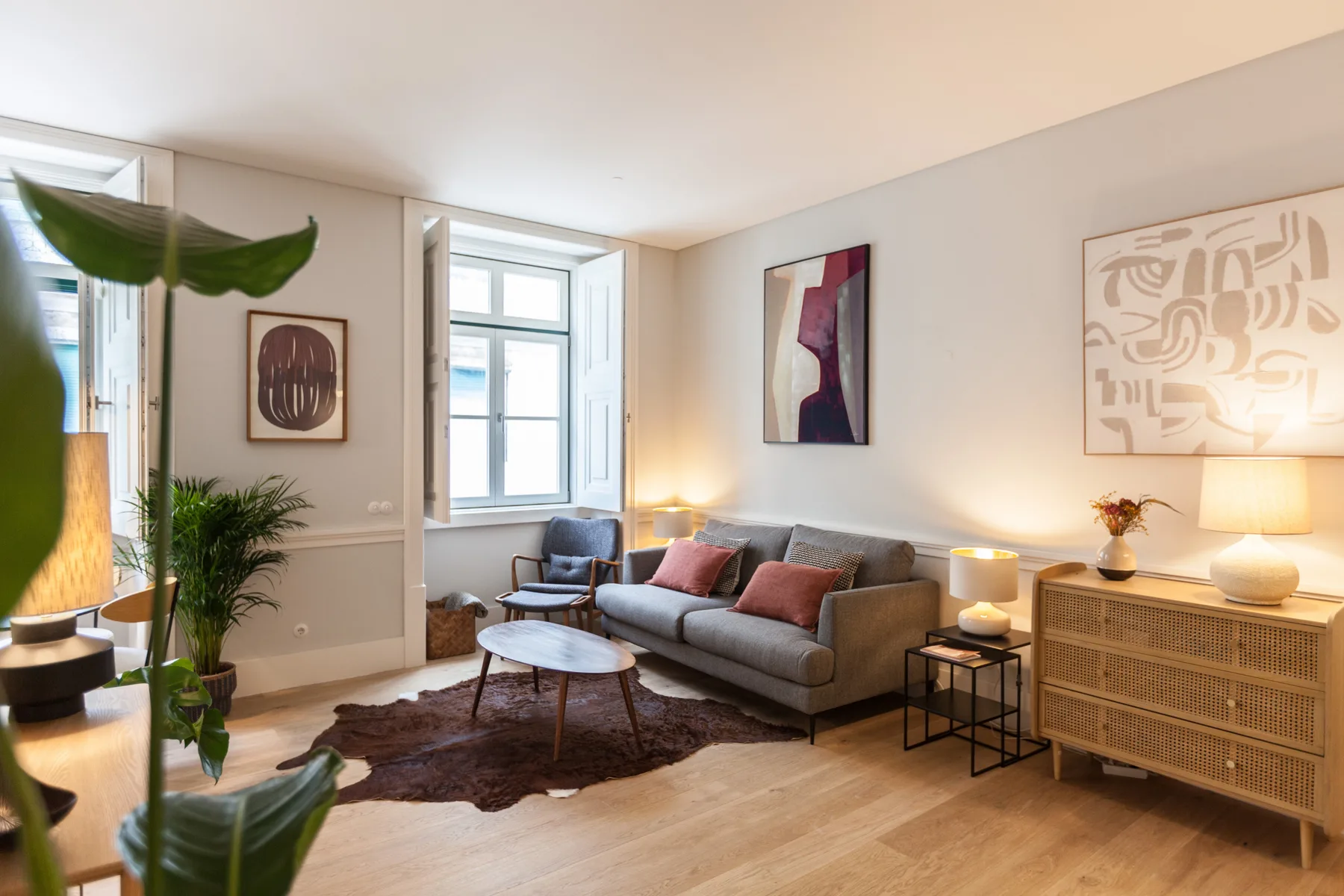 Una sala luminosa con un sofá gris, una mesa de centro y cuadros enmarcados.