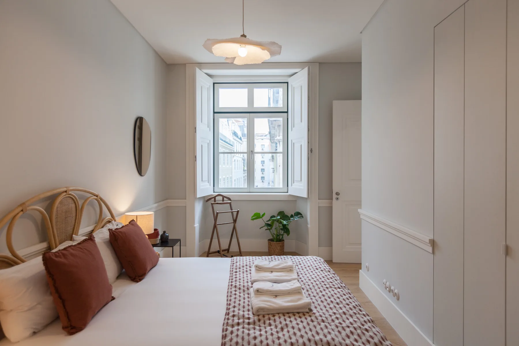 Un dormitorio con una cama, ropa de cama estampada y una ventana con vistas a edificios cercanos.