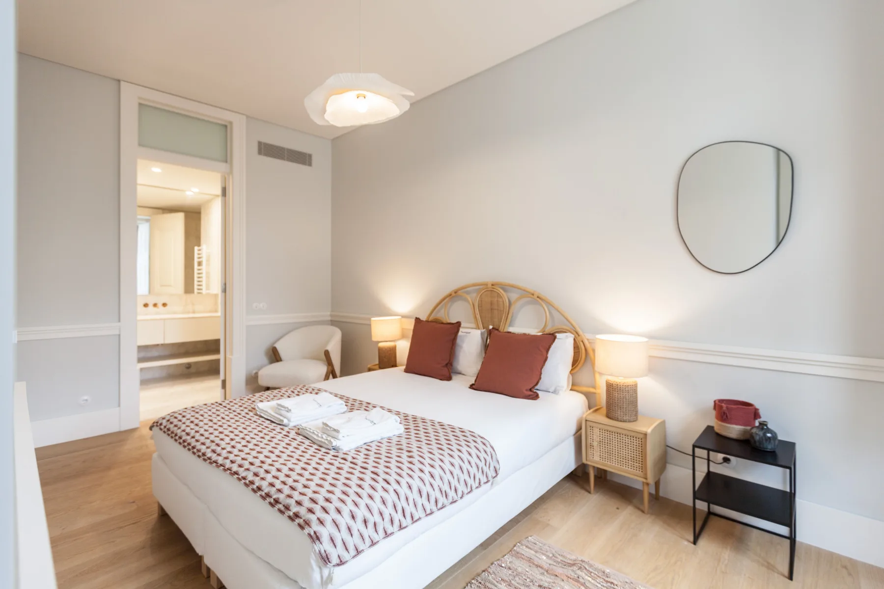Dormitorio con una cama, mesitas de noche y un espejo redondo en la pared.