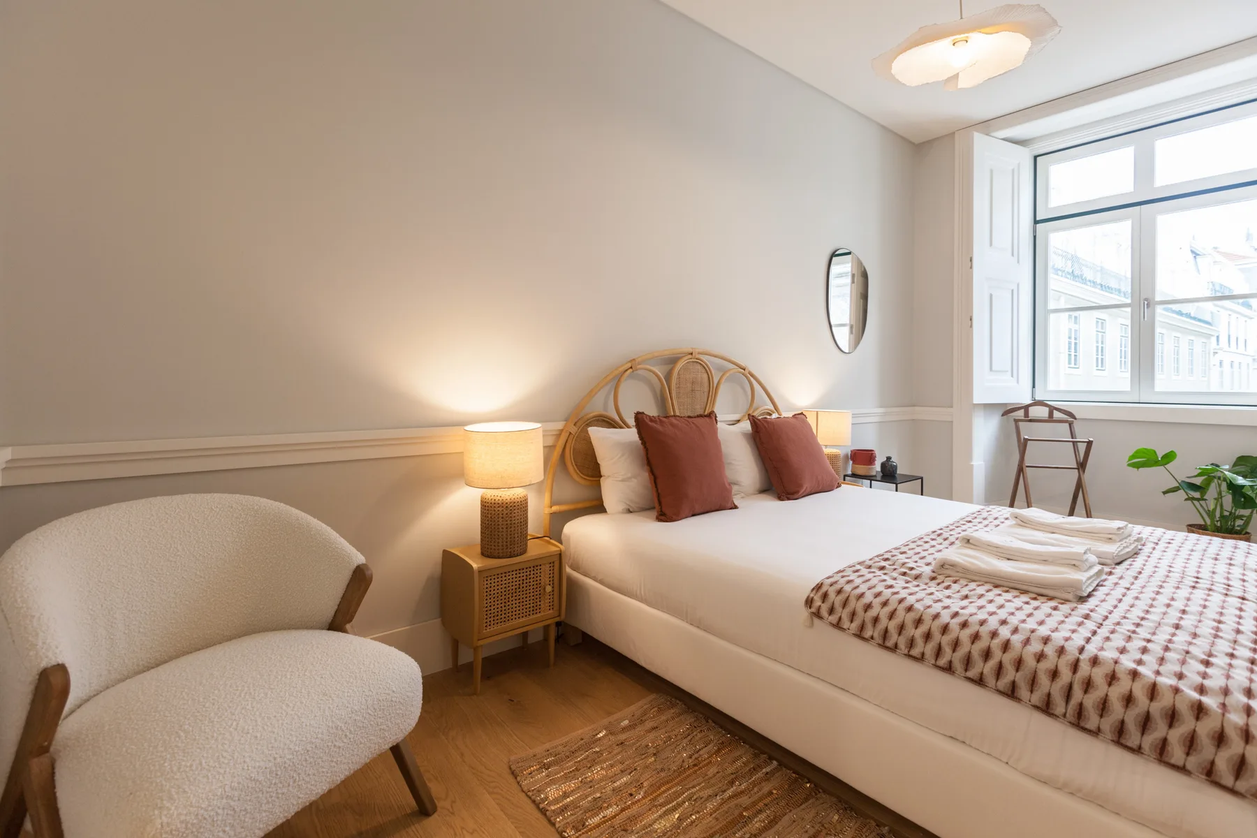 Un dormitorio luminoso con una cama doble, cabecero tejido y ventanas grandes.