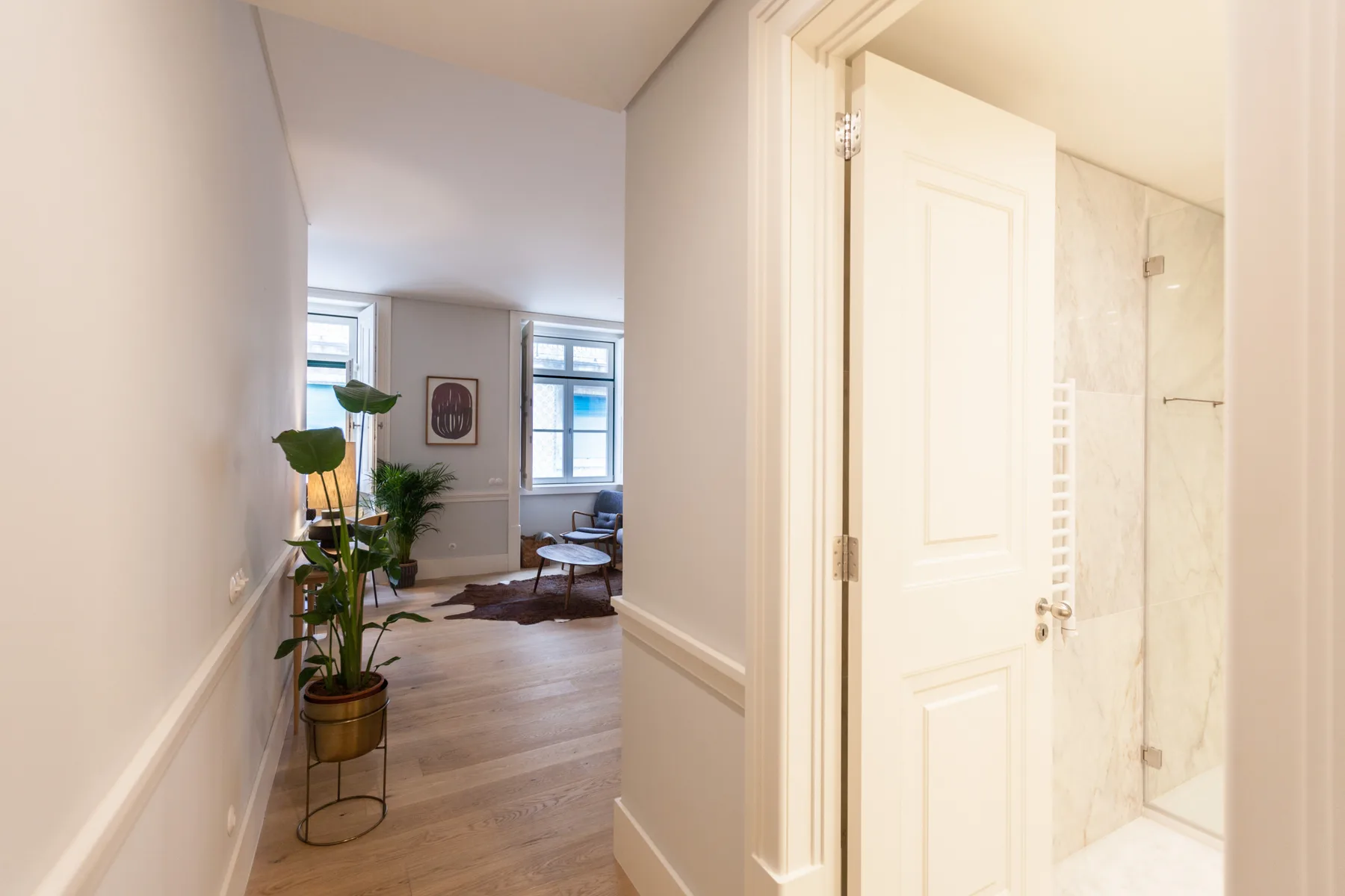 Un pasillo luminoso se abre a una zona de estar, con un baño visible tras una puerta abierta.