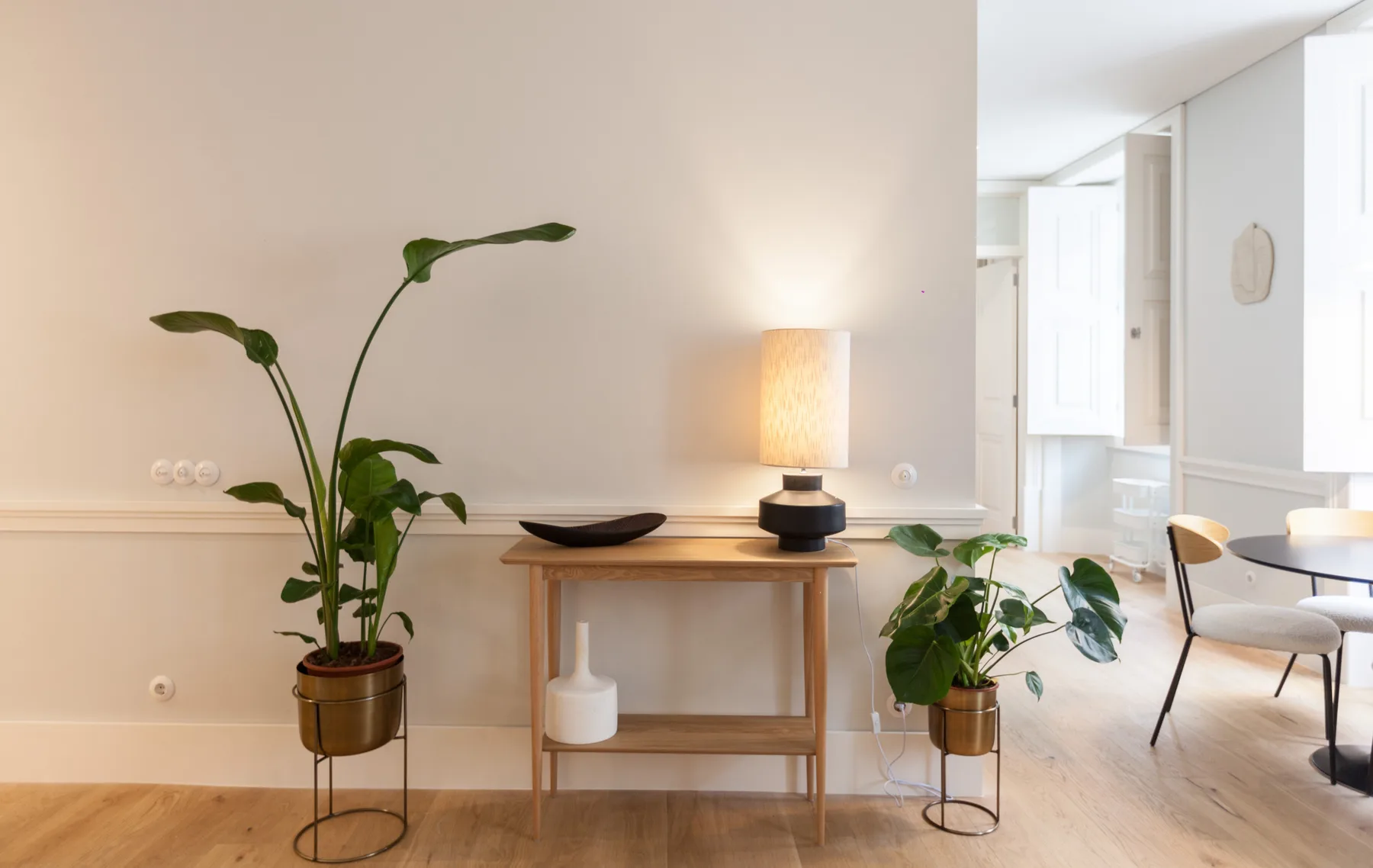 Una sala luminosa con una mesa consola, una lámpara y plantas junto a un comedor.