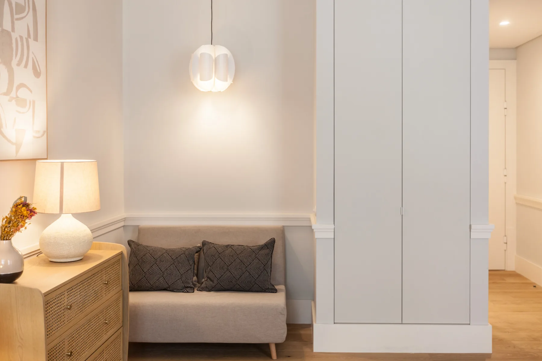 Una sala de estar con un sofá pequeño, un mueble y una lámpara colgante.