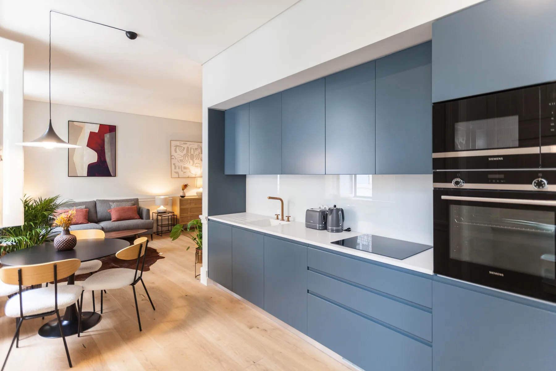Cocina y comedor modernos de planta abierta, con armarios azules y una mesa.