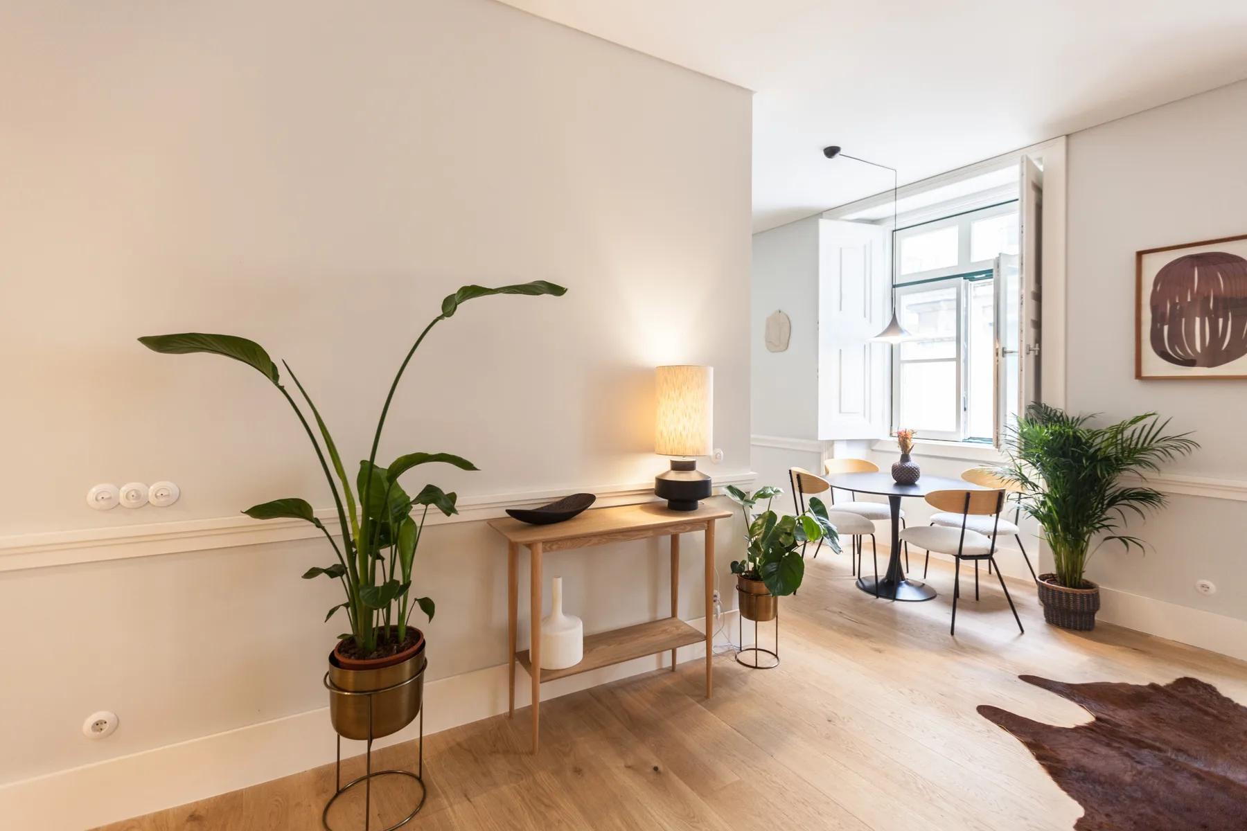 Luminoso espacio de estar y comedor con una mesa consola, asientos y plantas en macetas.