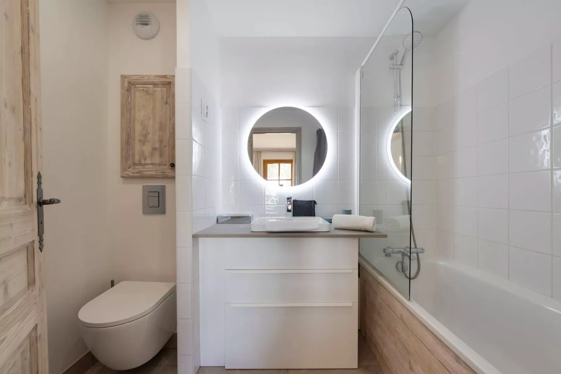 Un baño luminoso con lavabo, espejo redondo, inodoro y bañera.