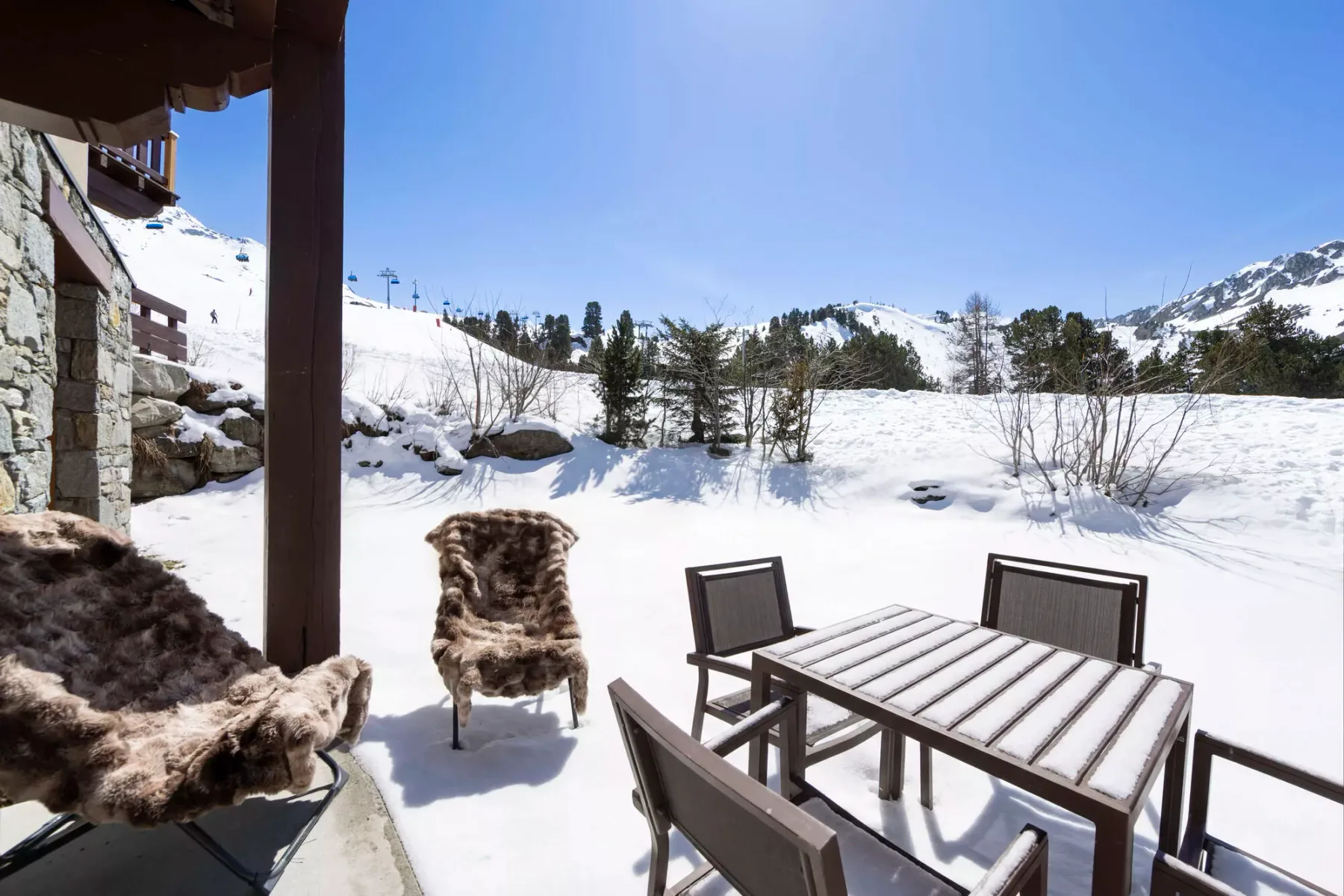 Un patio exterior nevado con mesa y sillas, frente a un paisaje montañoso.