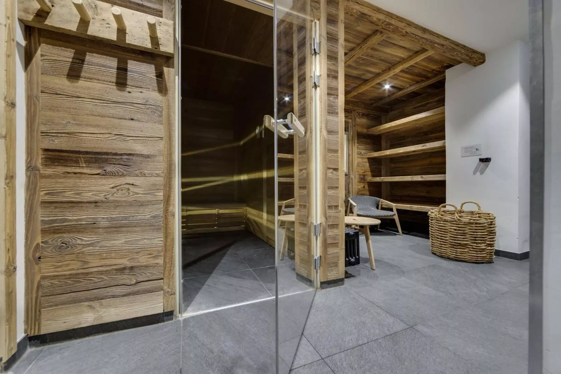 Una zona de sauna revestida de madera da a una sala embaldosada con asientos y cestas tejidas.