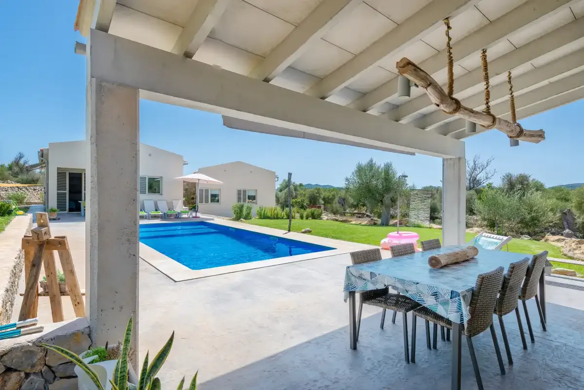 A covered patio overlooks a swimming pool beside a modern house.