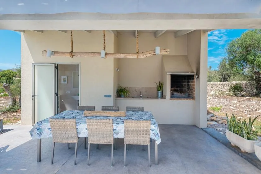 A covered outdoor dining area with a table and chairs beside a built-in grill.