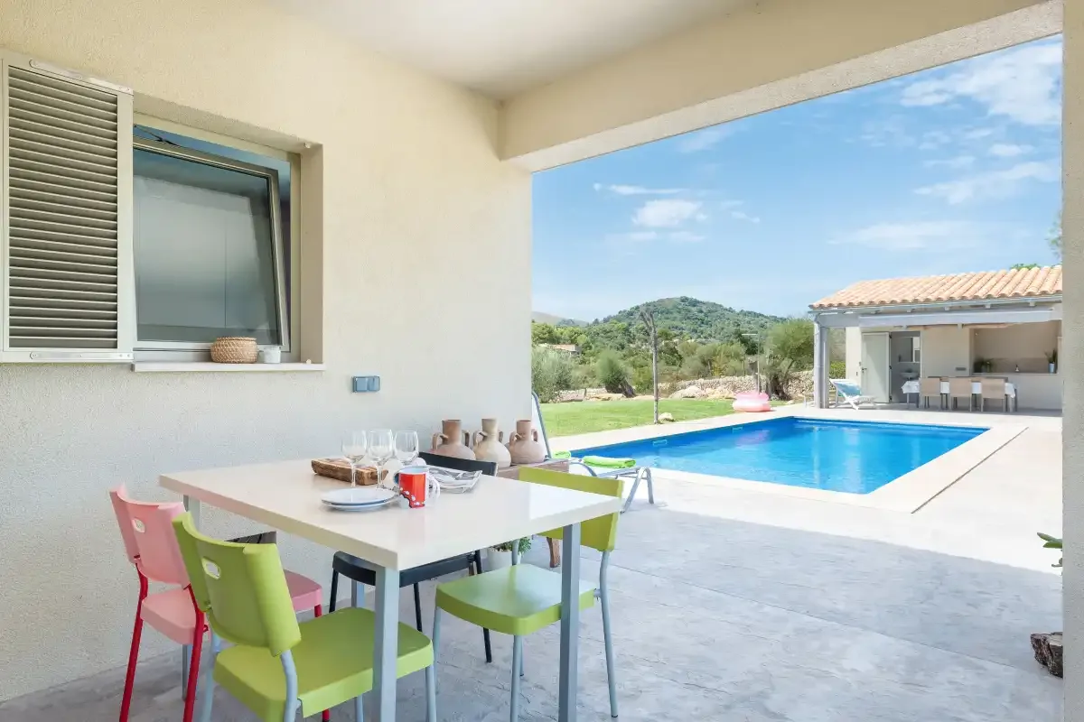 A covered patio dining area overlooks a swimming pool and surrounding hills.