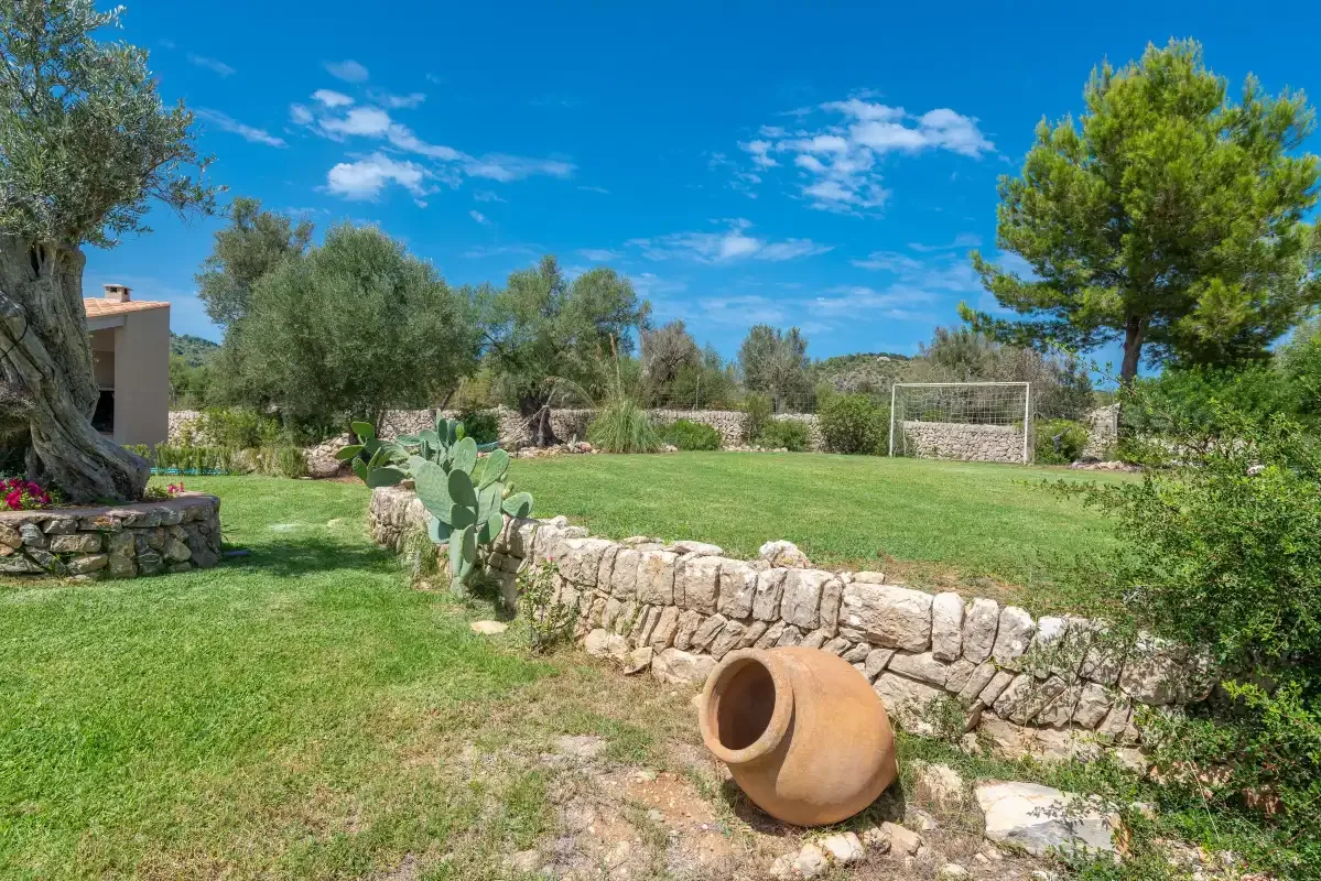 A grassy garden with a stone wall, trees, and a soccer goal.