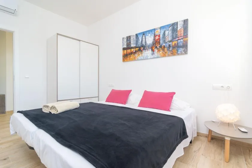 A bedroom with a large bed, pink pillows, and colorful cityscape artwork.