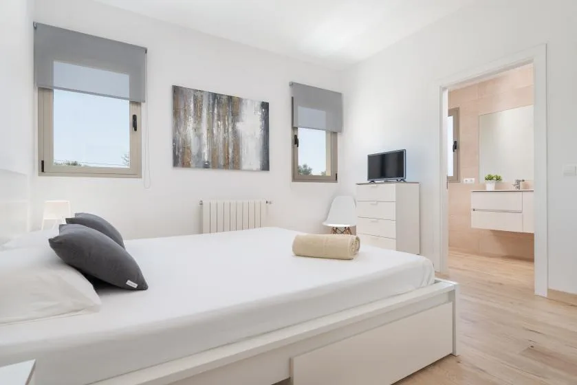 A bright bedroom with a neatly made bed and a doorway to the bathroom.