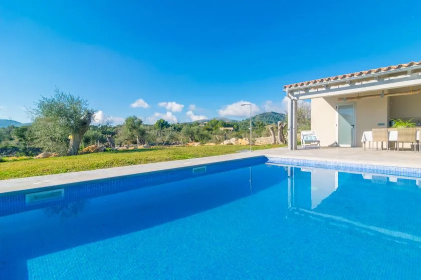 A swimming pool beside a covered patio, with green hills in the background.