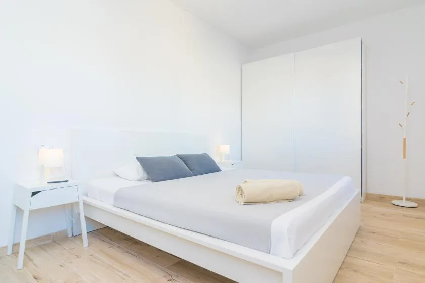 A bright bedroom with a neatly made bed and light wood flooring.