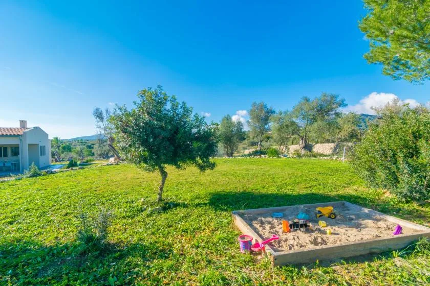 A grassy yard with a sandbox and trees under a clear blue sky.
