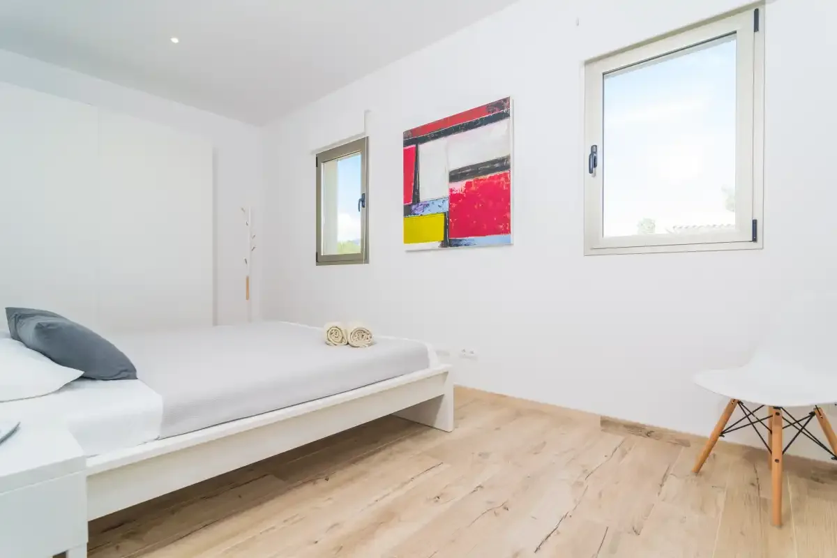 A bright bedroom with a low bed, colorful wall art, and two windows.