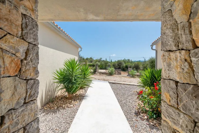 A white walkway leads through a stone entrance toward a landscaped outdoor area.