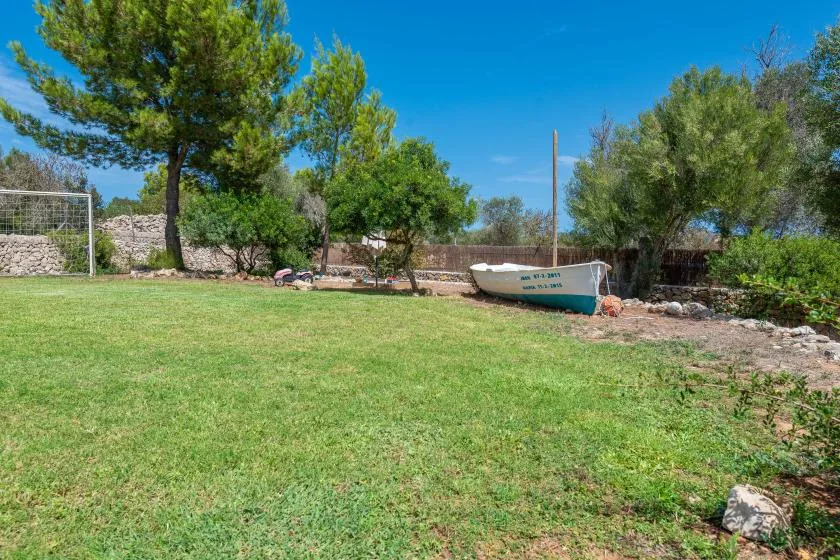 A grassy outdoor area with trees, a stone wall, and a small boat.