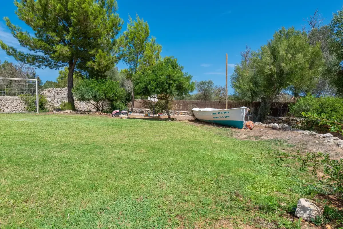 A grassy outdoor area with trees and a small boat beside a stone wall.