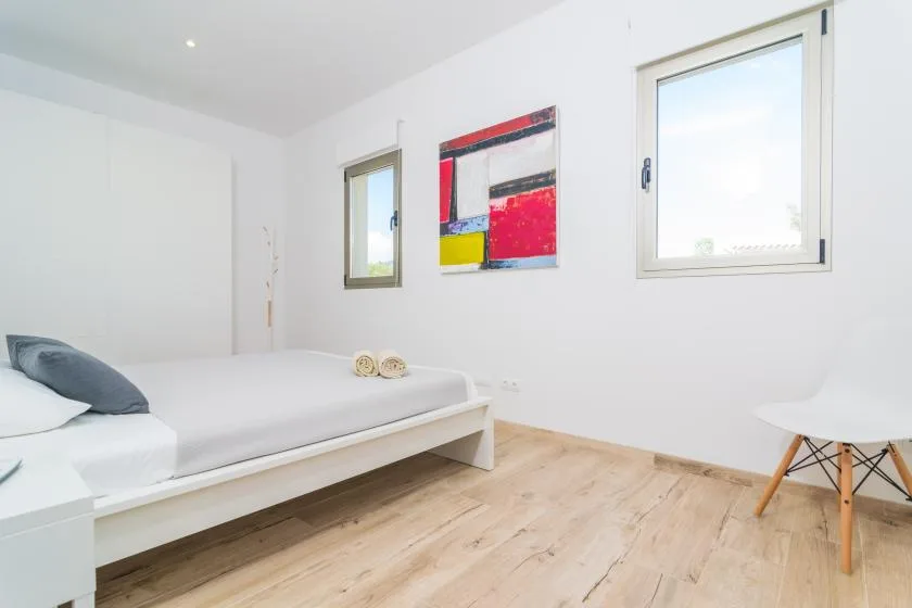 A bright bedroom with a low bed, colorful wall art, and two windows.