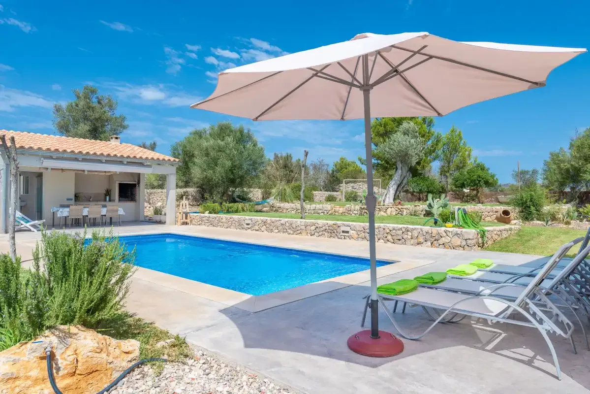An outdoor swimming pool beside a patio with lounge seating and a large umbrella.