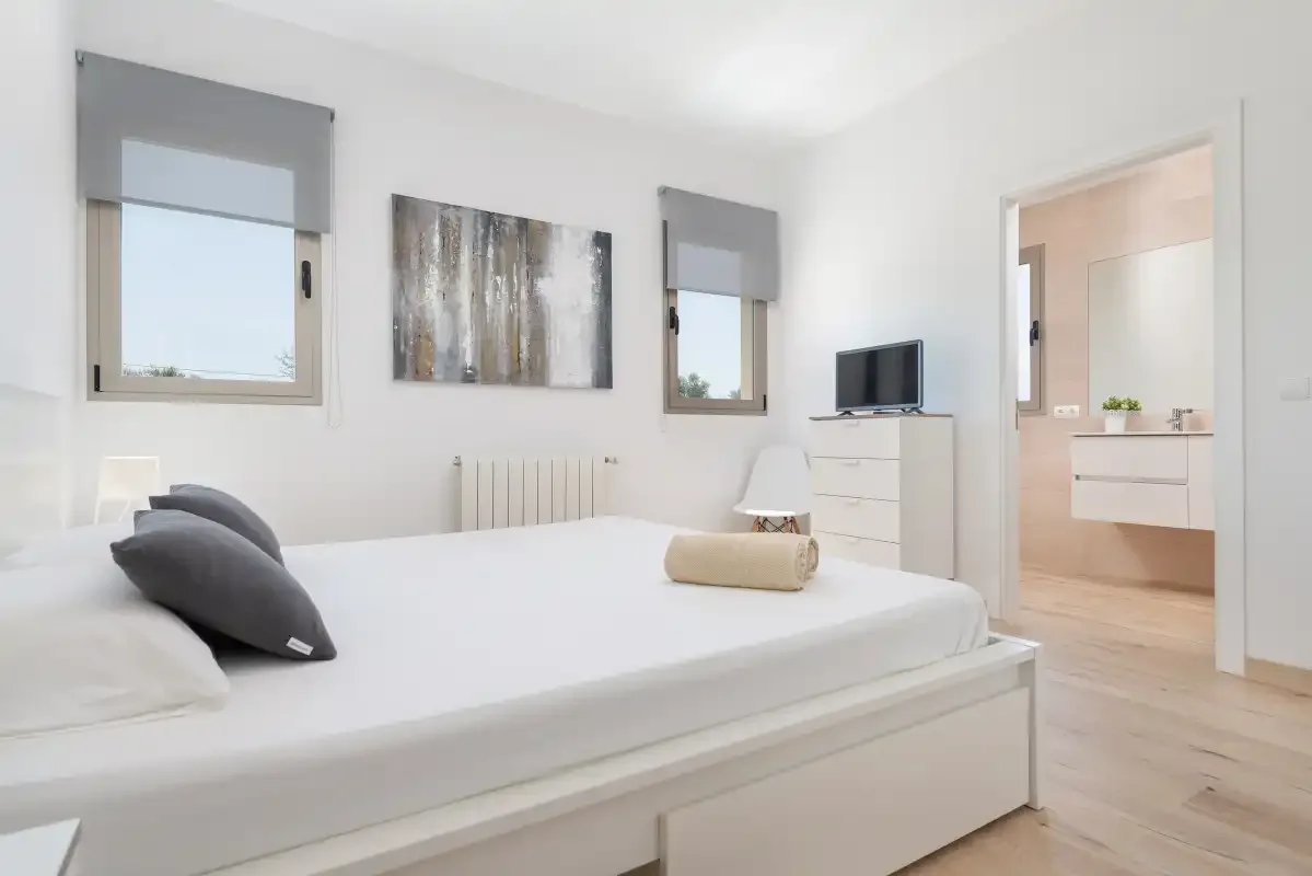 A bright bedroom with a bed, two windows, and an open doorway.