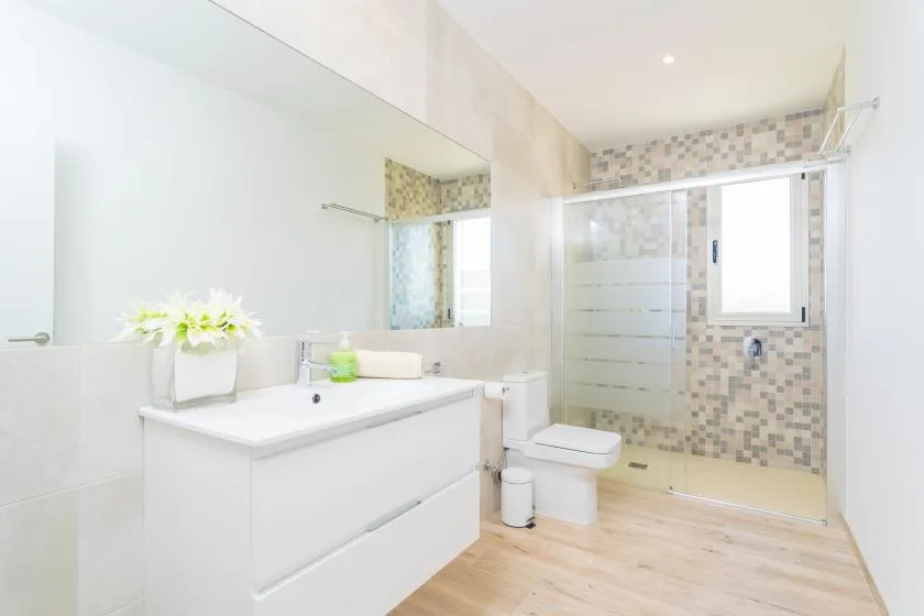 A bright bathroom with a long vanity, toilet, and glass shower.