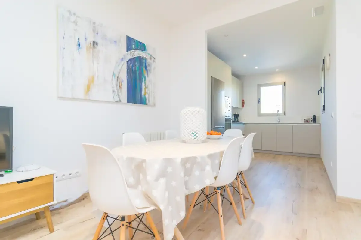A bright dining area opens onto a kitchen, with abstract artwork on the wall.