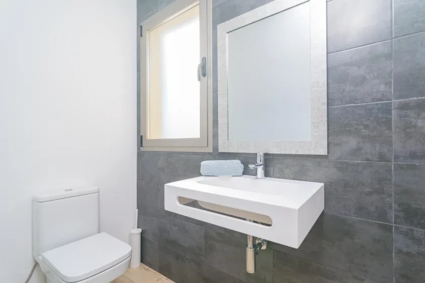 A bathroom with a wall-mounted sink, mirror, window, and toilet.