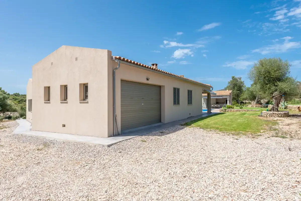 A single-story house with a large garage door sits beside a gravel driveway.