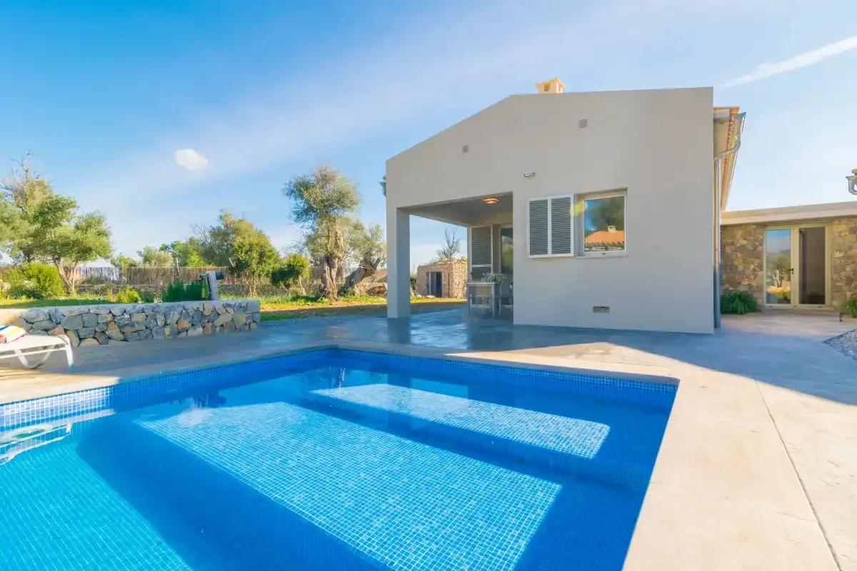 A swimming pool sits beside a modern house under a clear blue sky.