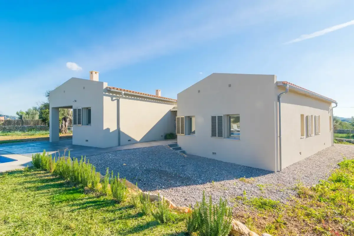 A modern house stands beside a swimming pool, with gravel and greenery around it.