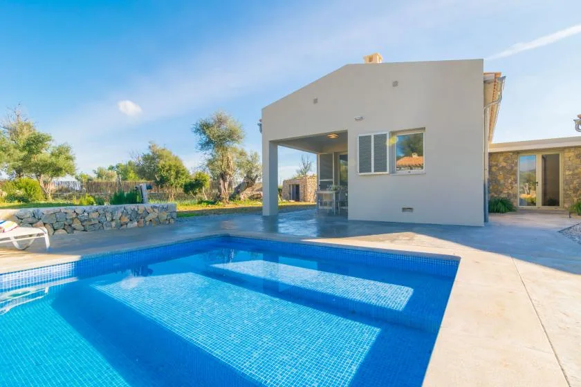 A swimming pool sits beside a modern house under a clear blue sky.