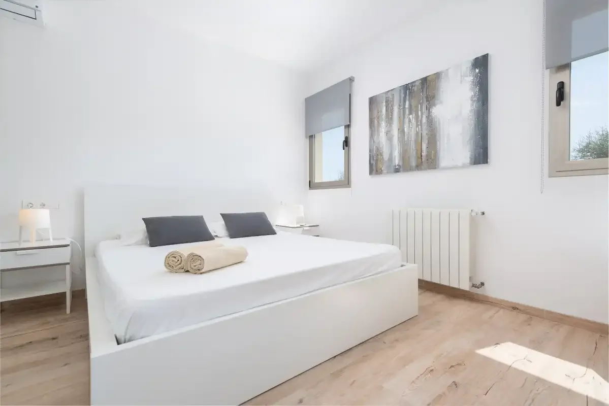 A bright bedroom with a neatly made bed, bedside tables, and wall art.