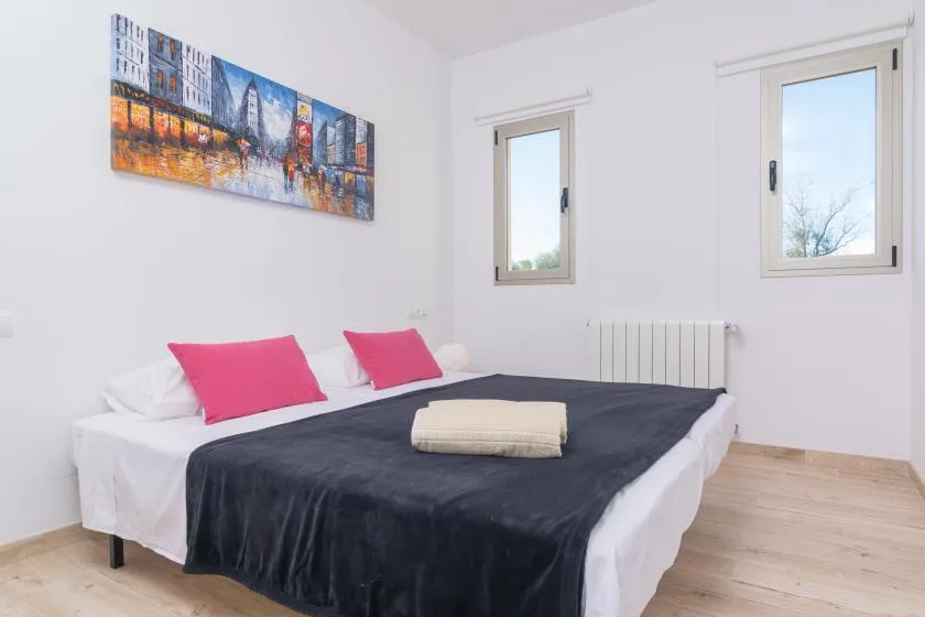 A bedroom with a bed dressed in dark bedding and two bright pink pillows.