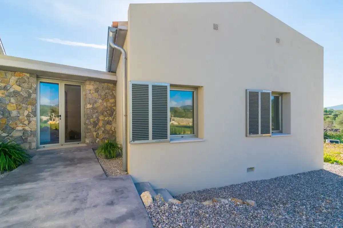 A modern house exterior with shuttered windows and a stone wall.
