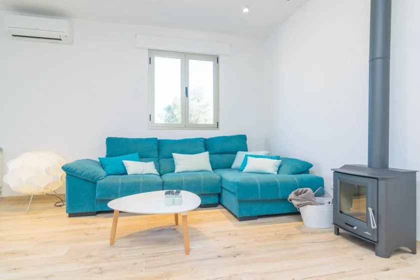 A bright living room with a teal sectional sofa and a wood-burning stove.