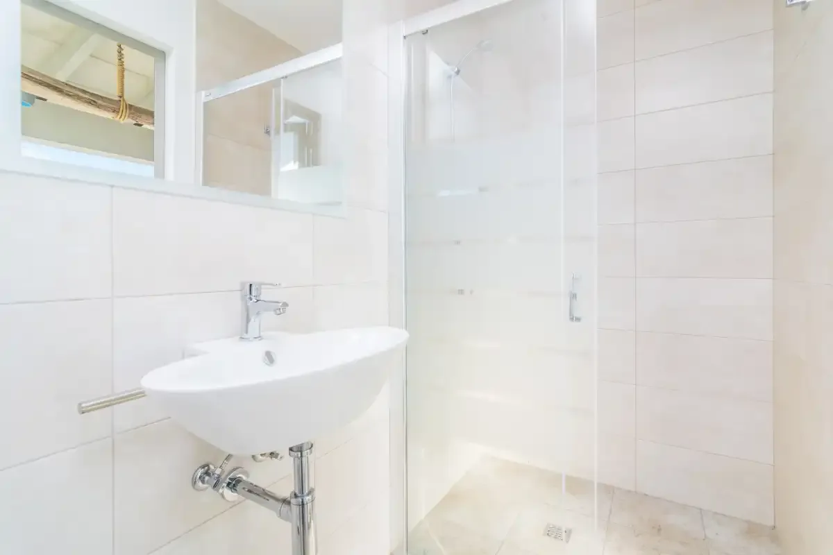 A bright tiled bathroom with a wall-mounted sink and glass shower.
